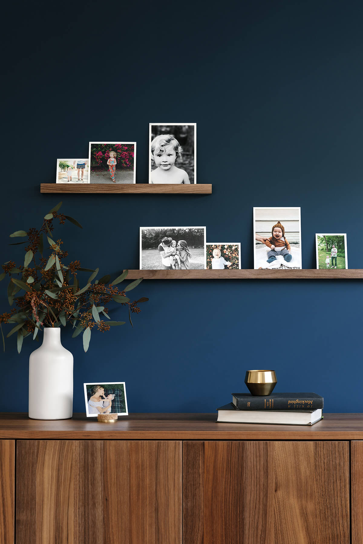 Photo prints of children on display on two floating shelves attached to a dark blue wall