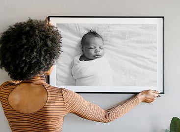 Woman hanging large portrait of swaddled newborn baby up on wall