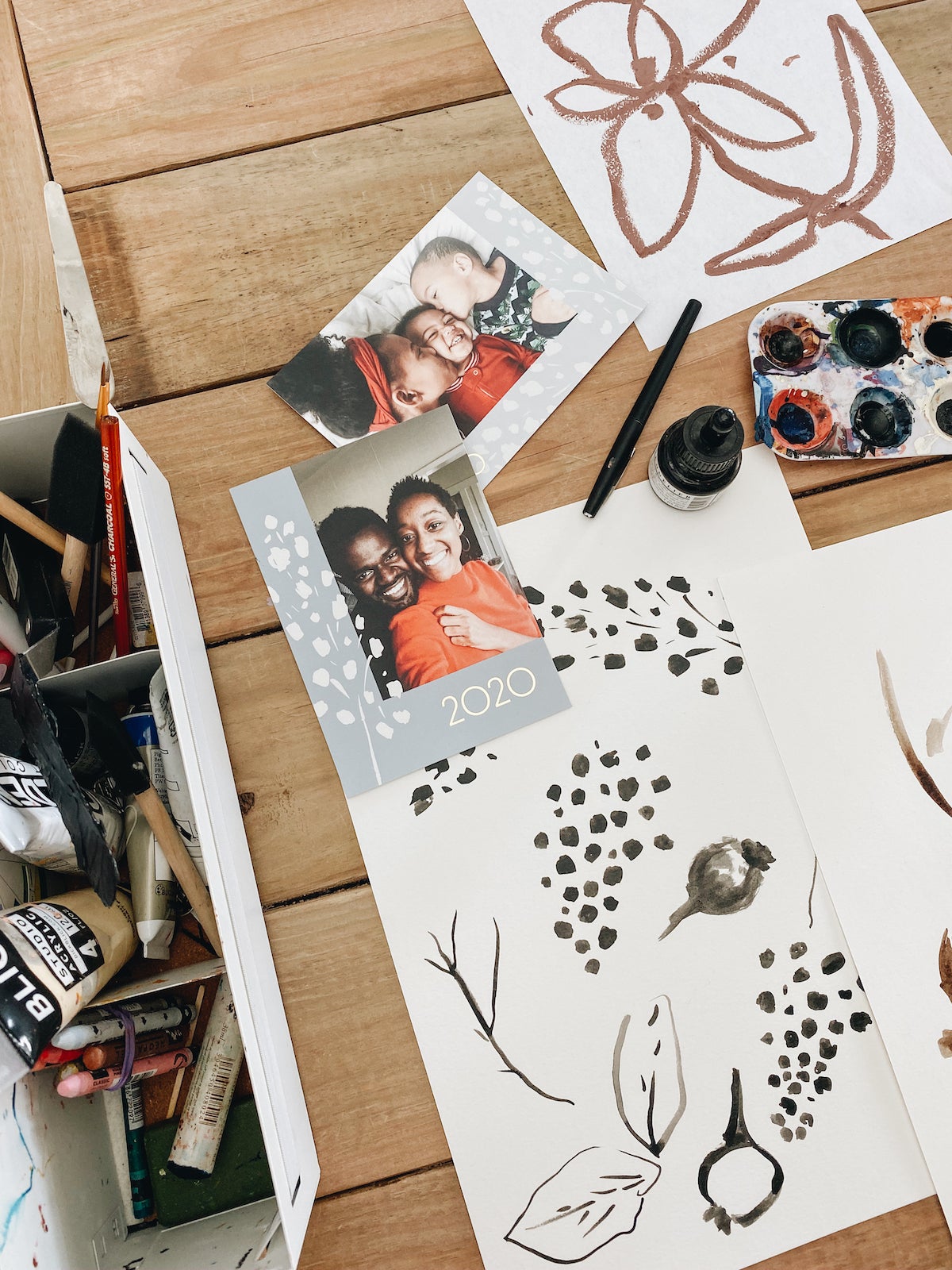 Holiday cards and drawings spread out on a studio table with art supplies
