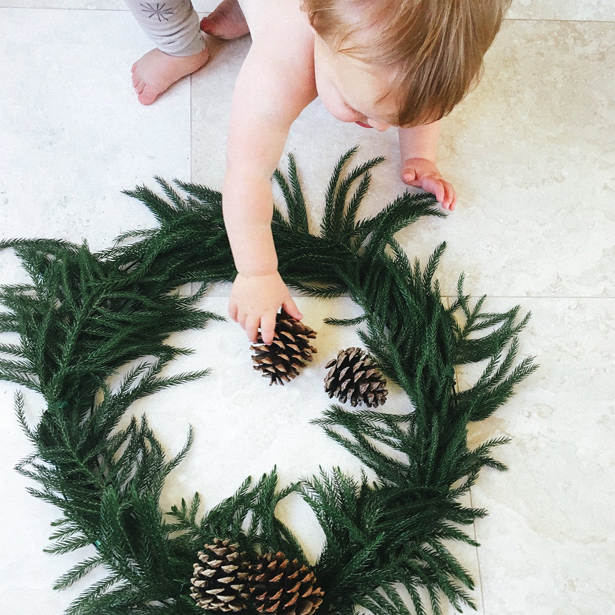 Toddler placing pinecone on homemade wreath