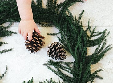 Child's hand placing pinecone inside of wreath on the floor