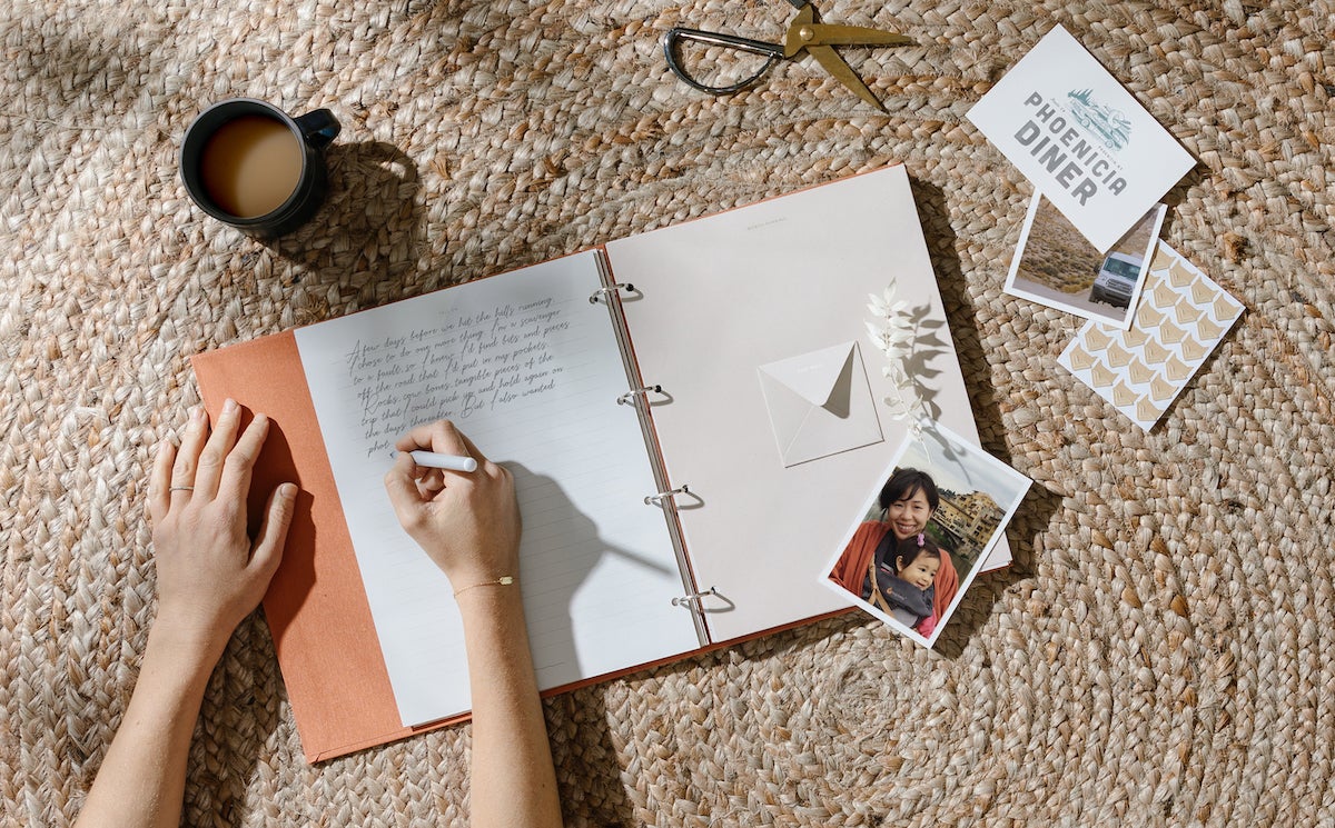 Woman writing in scrapbook with keepsakes lying around the album