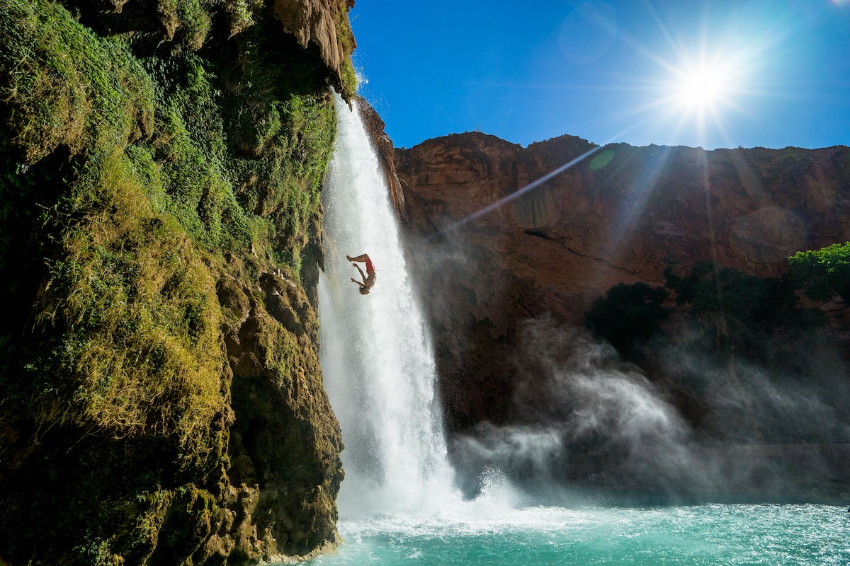 Man cliff diving next to waterfall in tropical setting