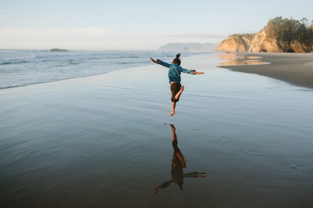 photo of child running and jumping along the coast