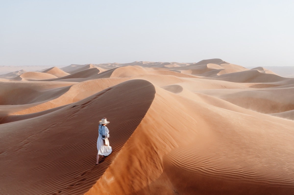Woman standing atop a sand dune peering out into the desert in Oman