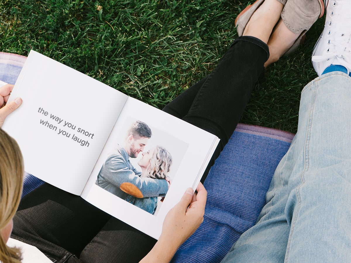 Couple flipping through Softcover Photo Book opened to photo of laughing couple