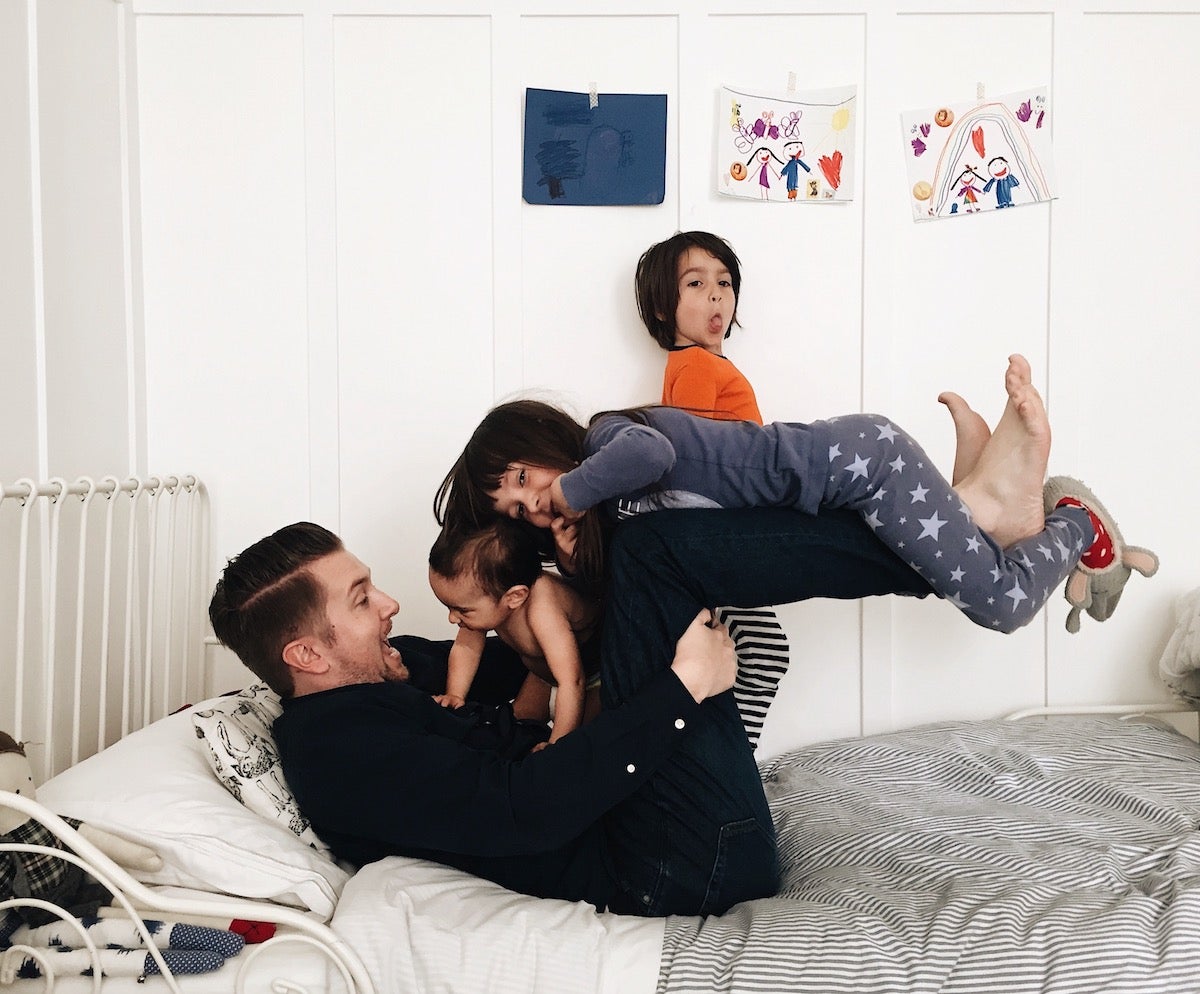 Father playfully wrestling with children on bed