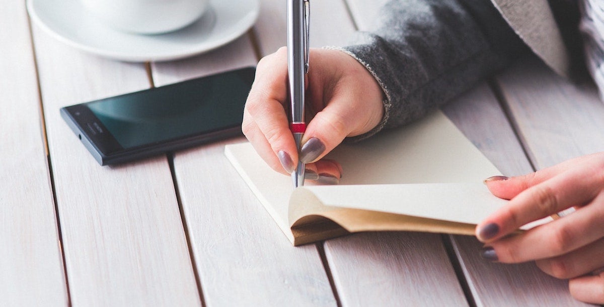 Woman's hand writing in journal with pen
