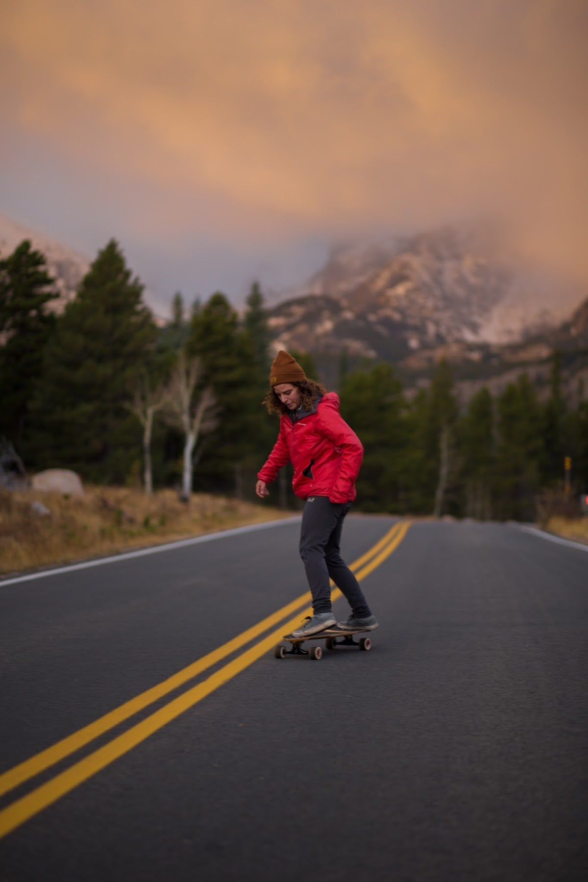 Skateboarder riding downhill on mountain road with snowy peaks in the background