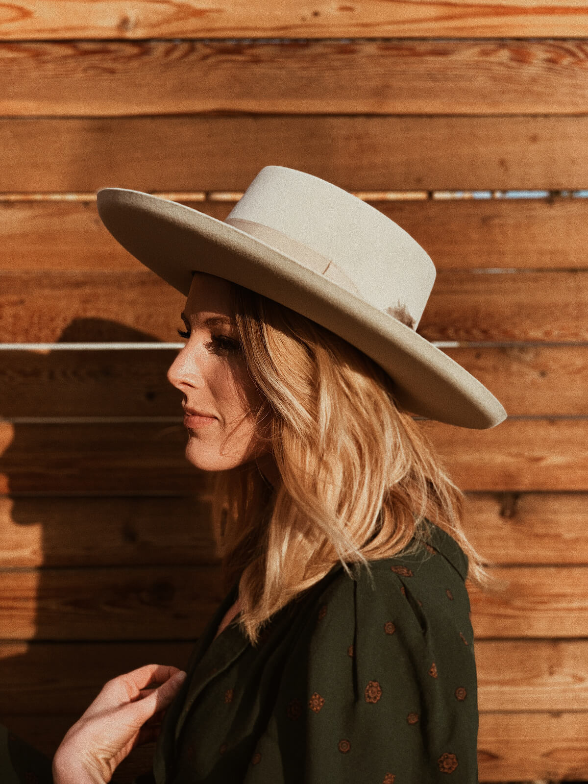 Side profile of young woman in hat in front of wood fence