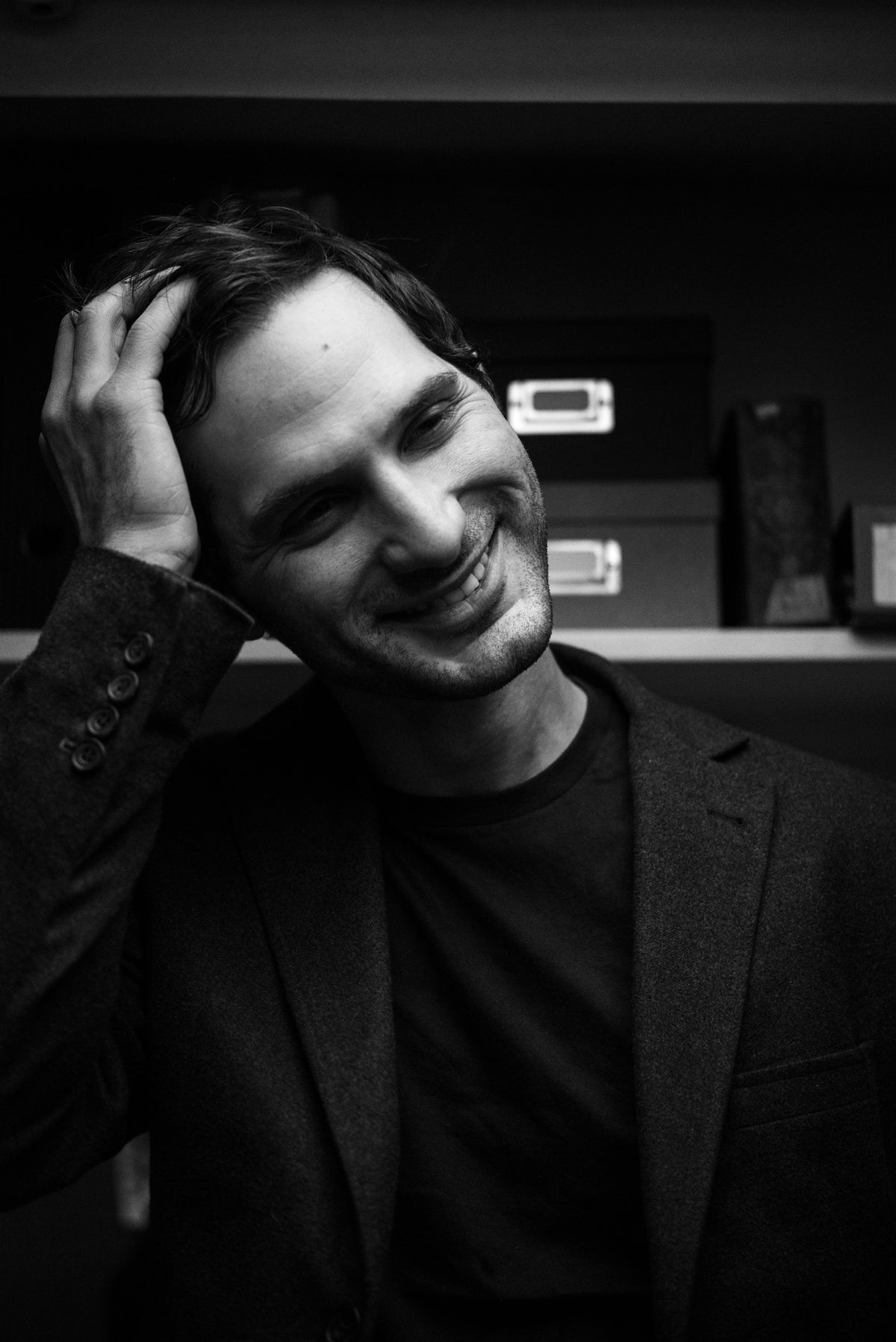 Black and white photo of young man laughing and tilting head to the side as he slicks back hair