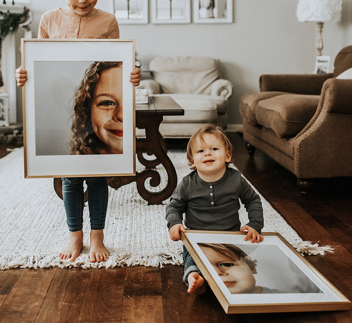 Two young siblings hold up enlarged and framed photos of themselves