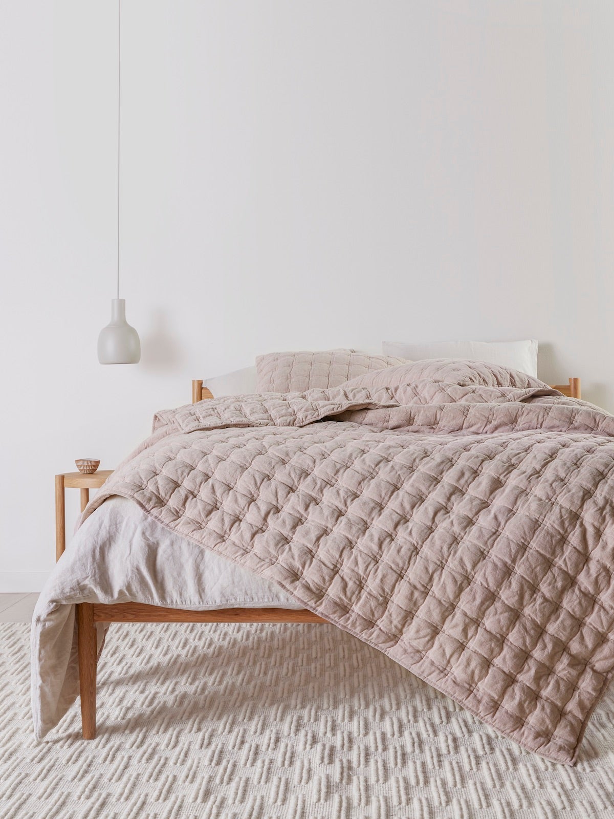 Quilted blush bedspread on unmade bed