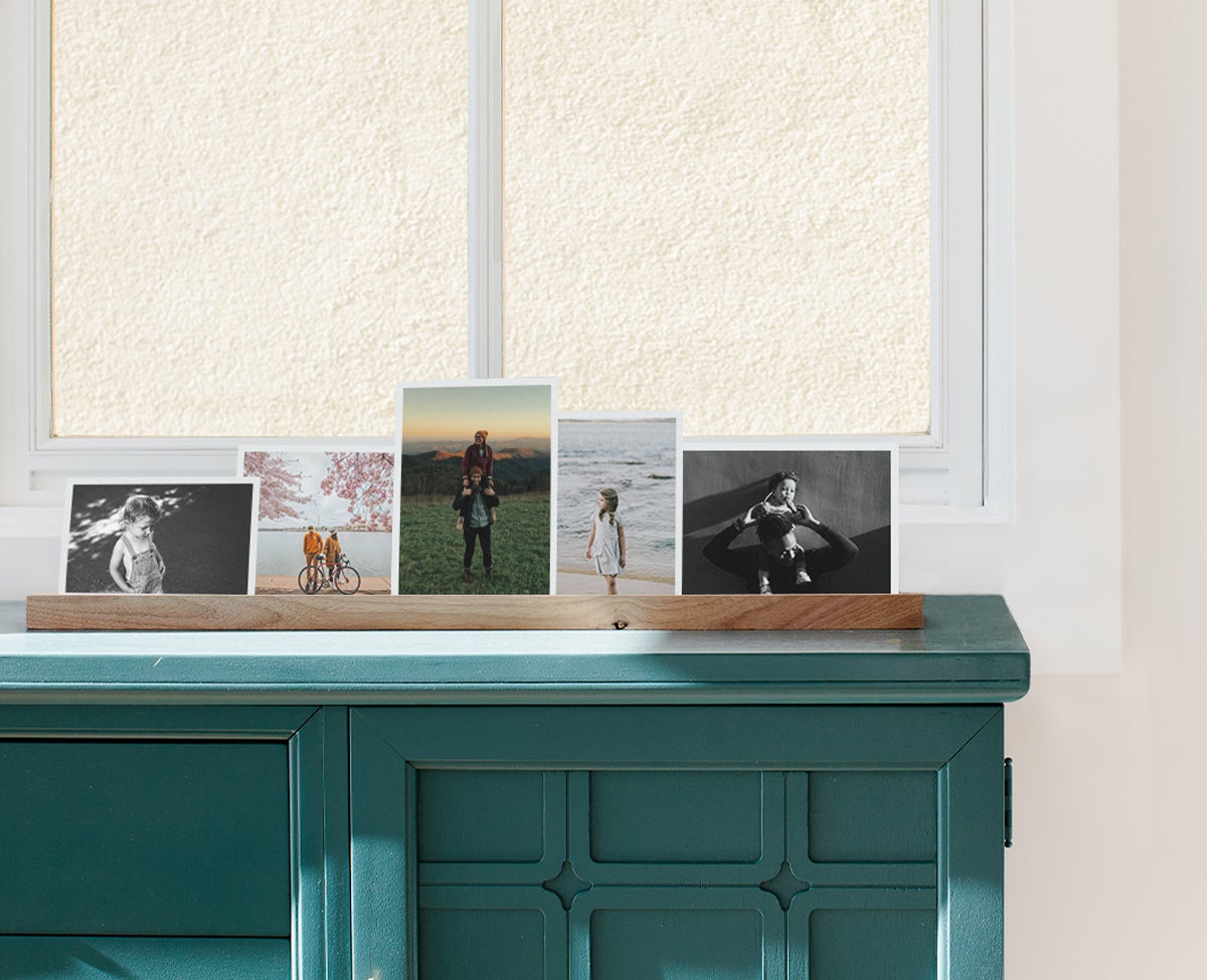 Wooden photo ledge standing on dresser and lined with prints