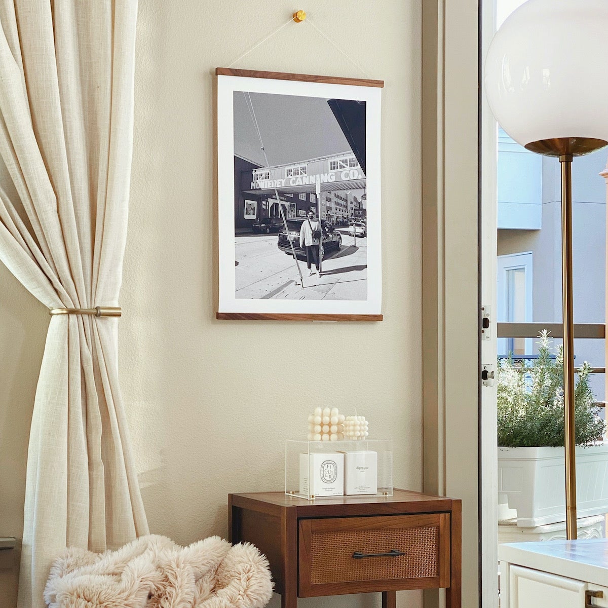 Large Artifact Uprising print featuring photo of man in front of old canning company hanging from print hanger in corner with nightstand