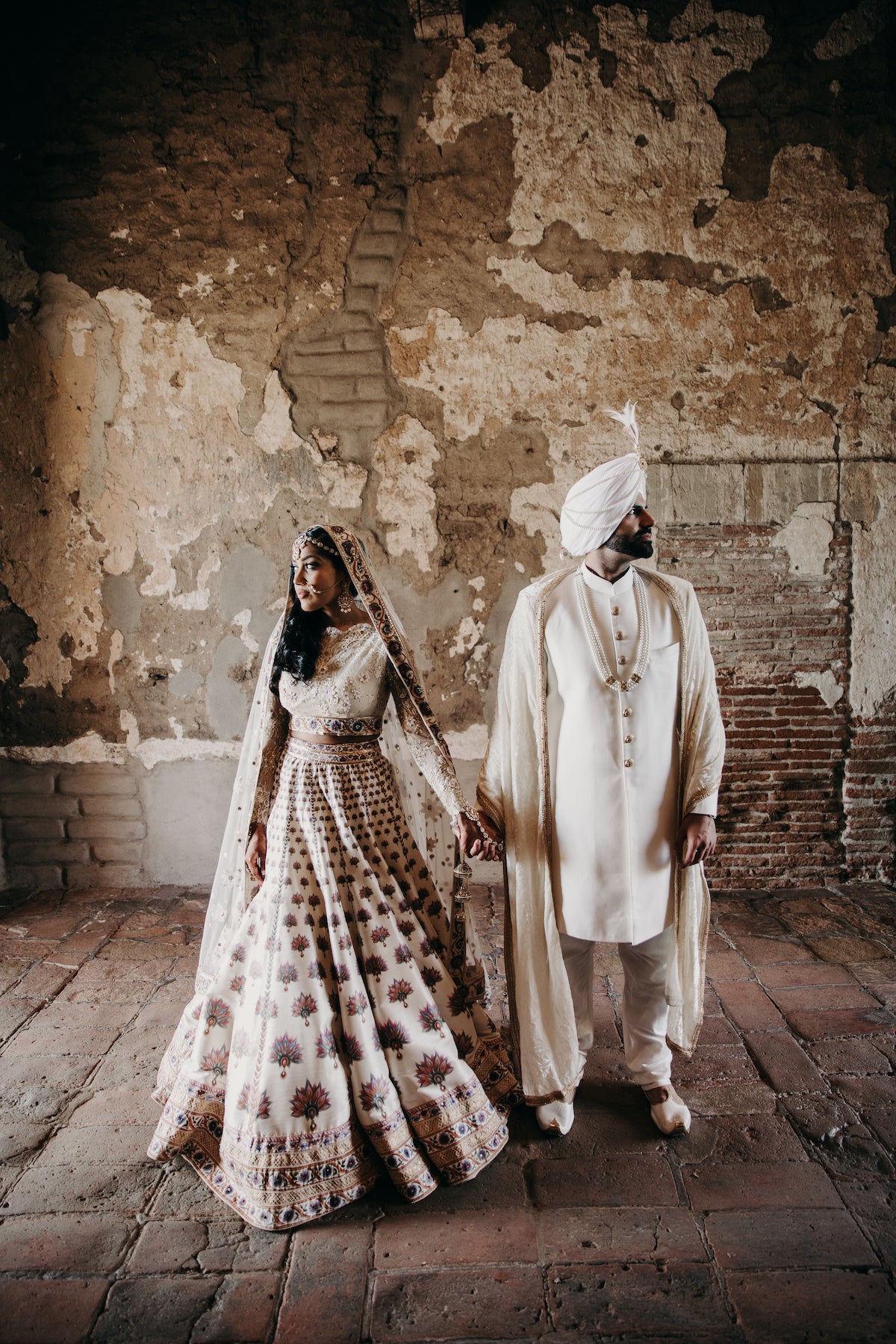 Couple in traditional cultural wedding attire standing in front of artsy brick wall
