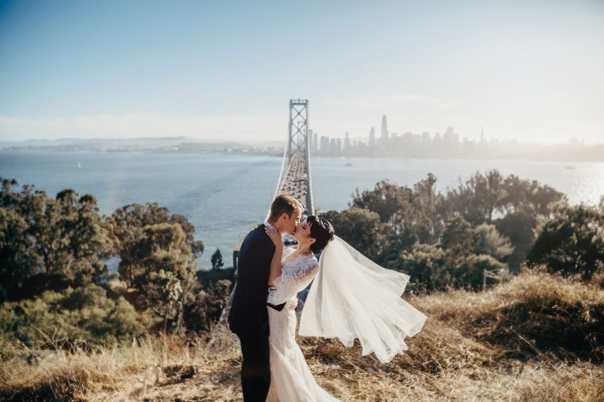 Bride and groom kissing with bridge and city in background