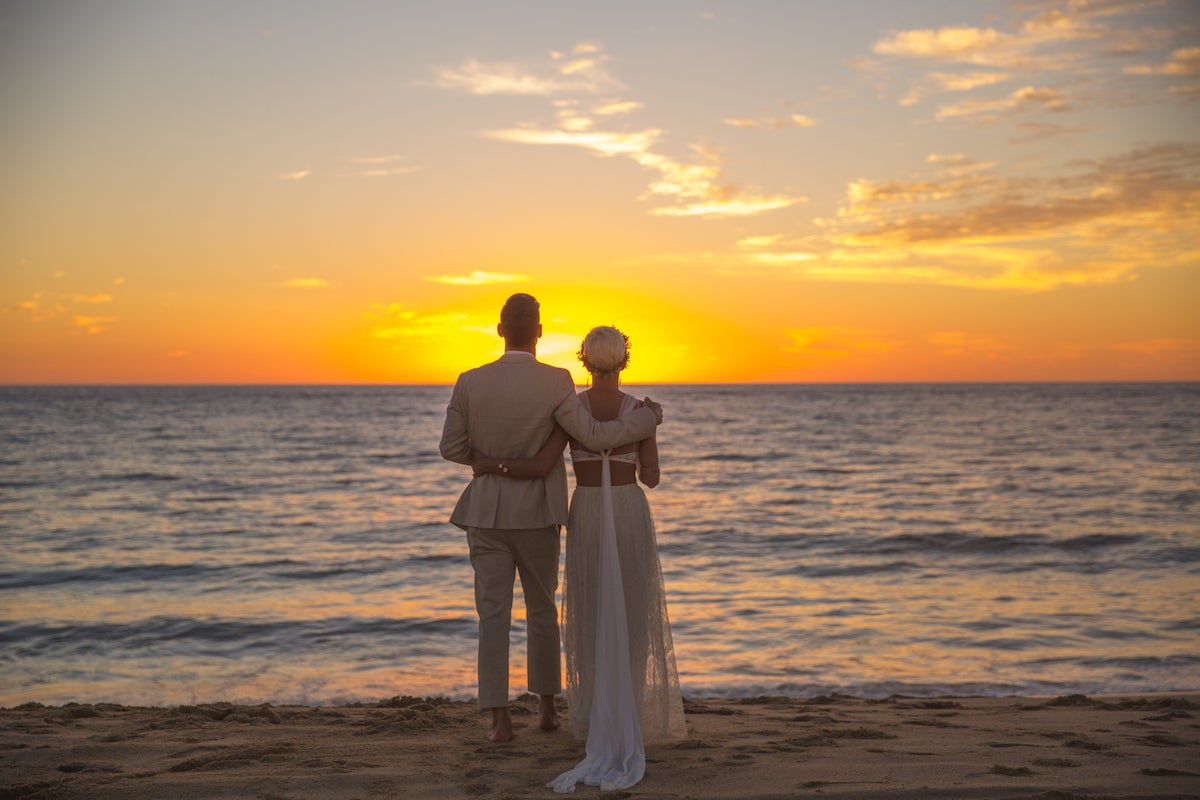 Bride and groom watching the sun set over the ocean