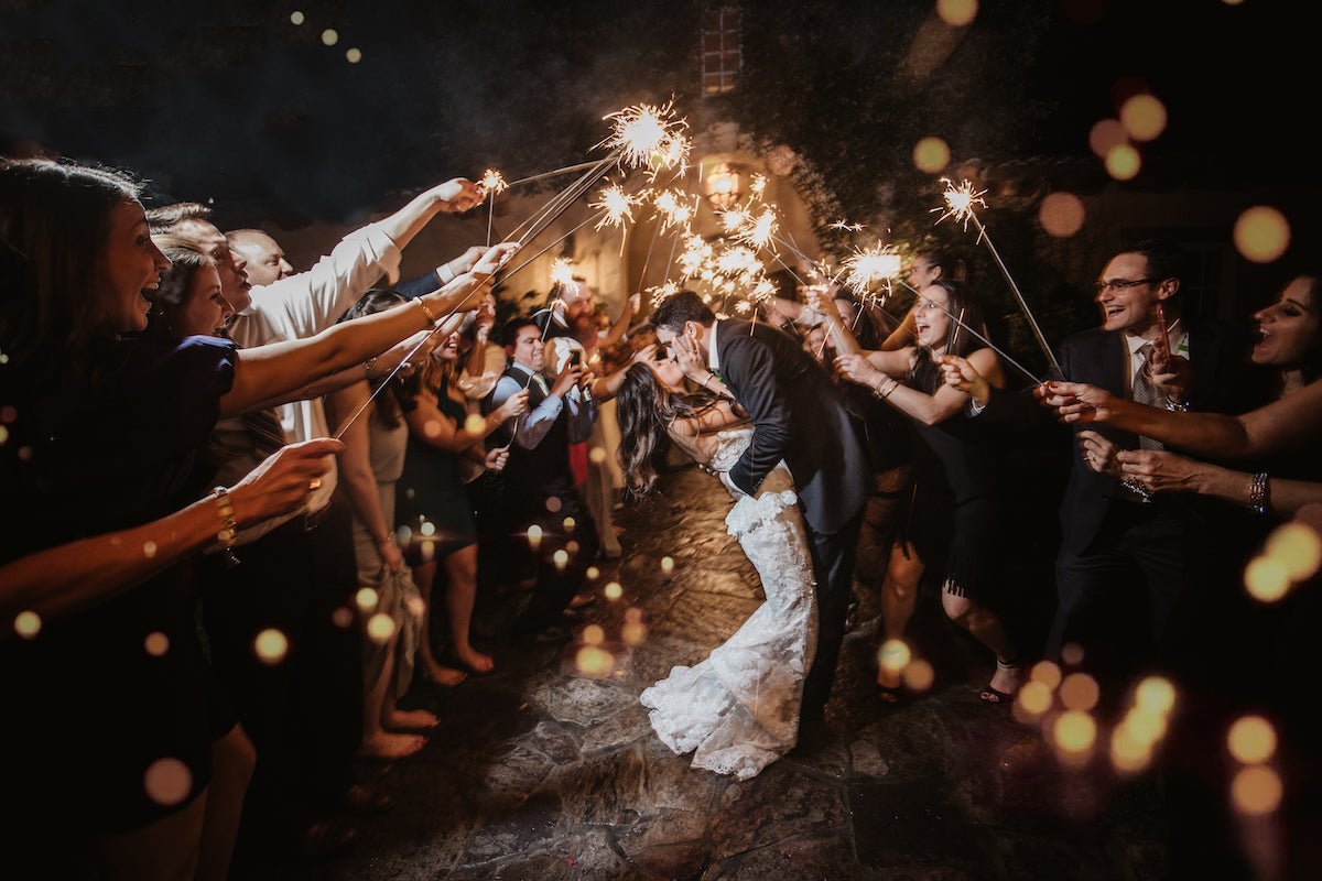 Bride and groom kissing in tunnel of guests holding sparklers