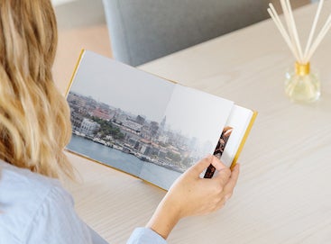 Woman flipping through honeycomb travel album opened to two-page cityscape