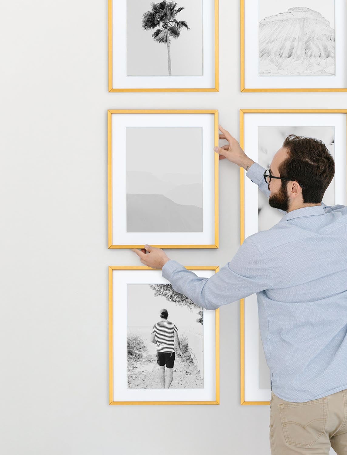 Man hanging framed black and white photo to complete gallery wall