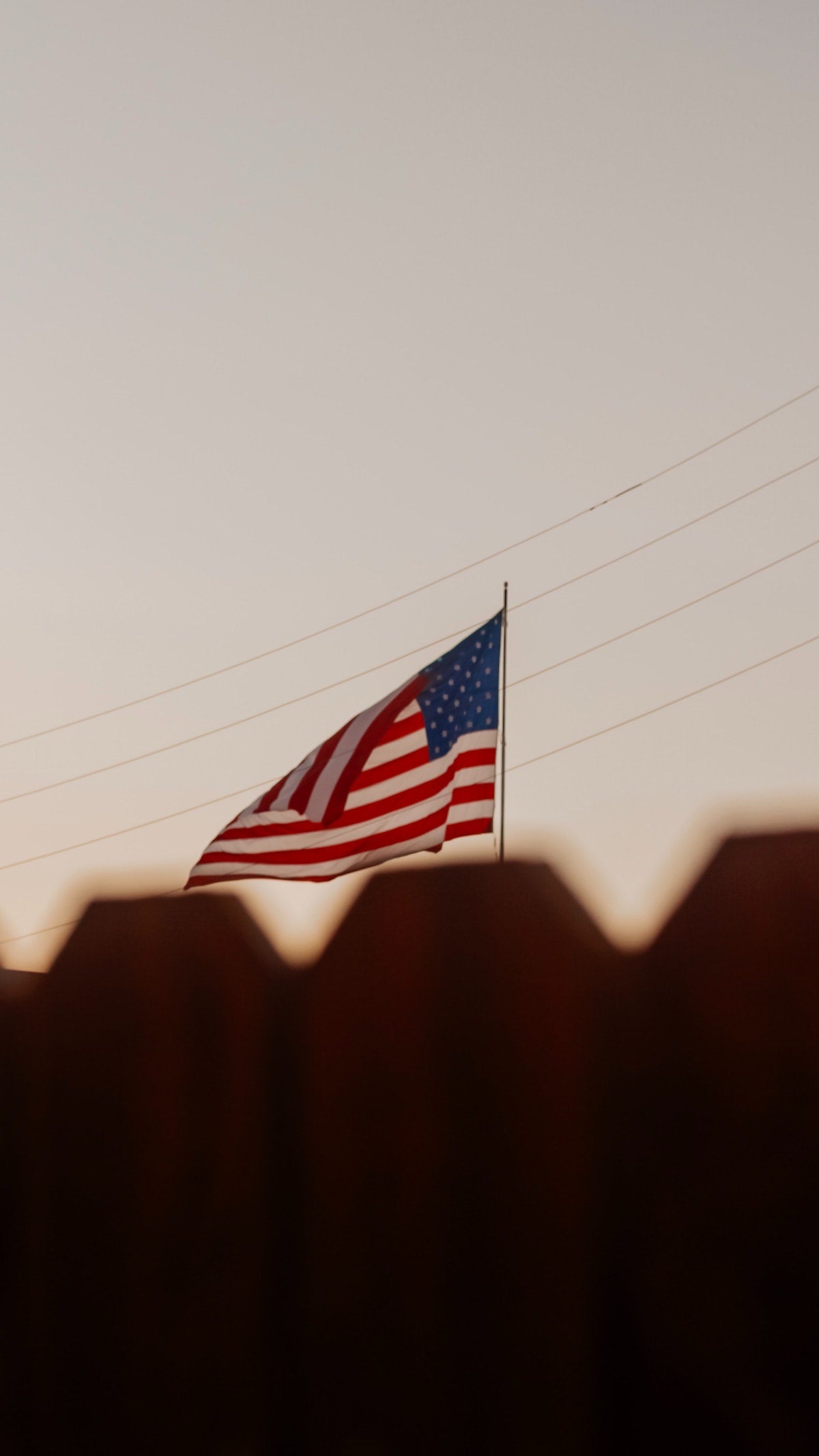 A photo of the American flag displayed just above the top of a fence in the foreground