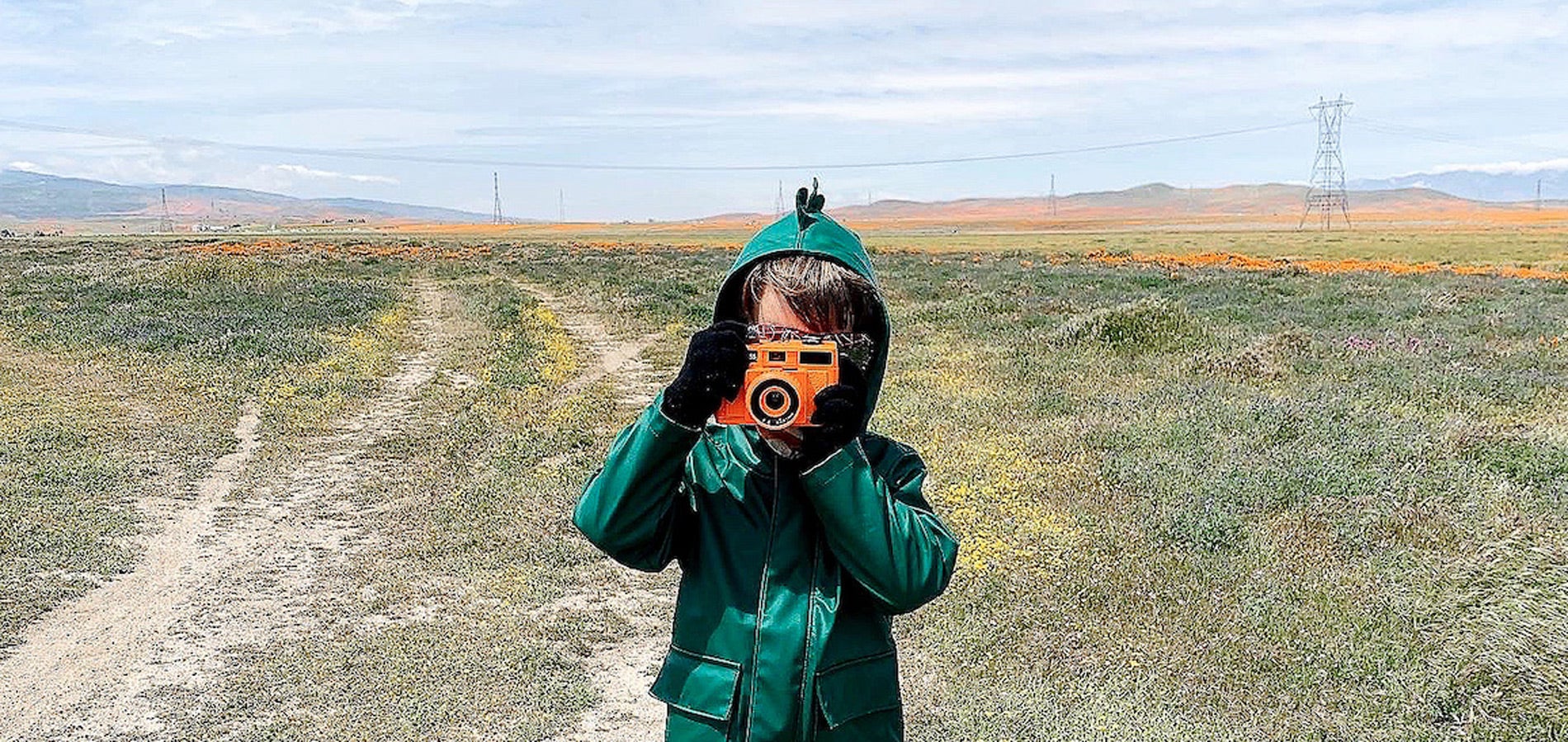 Child pointing camera at camera while standing in open pasture