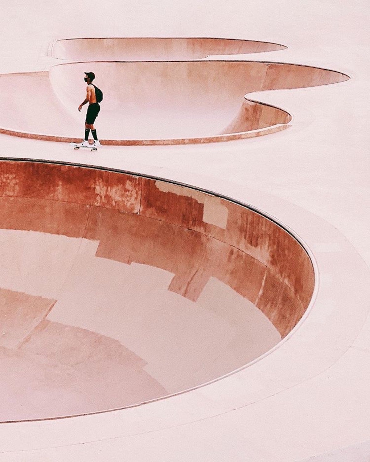 A skateboarder riding between two skate bowls with a red filter on the shot