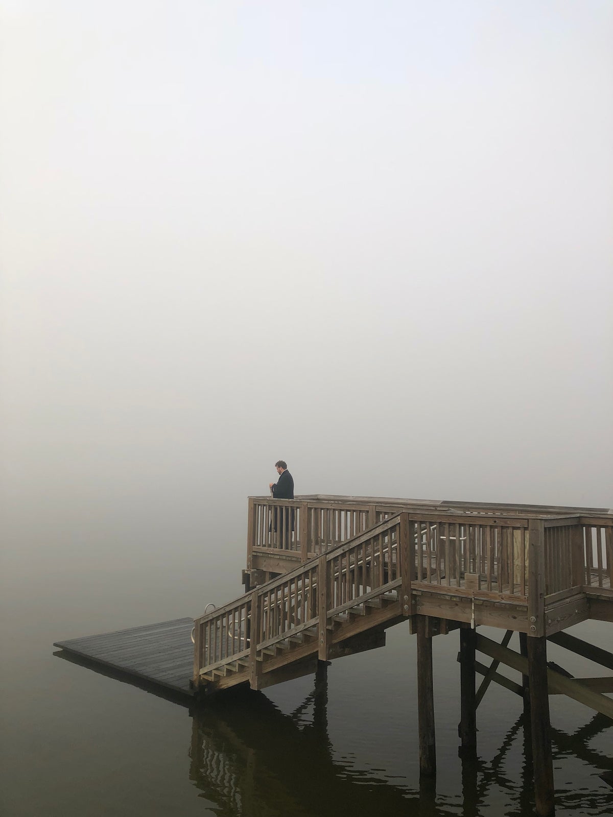 A dock in the water with a wooden walkway with a man staring over the edge in to the beyond