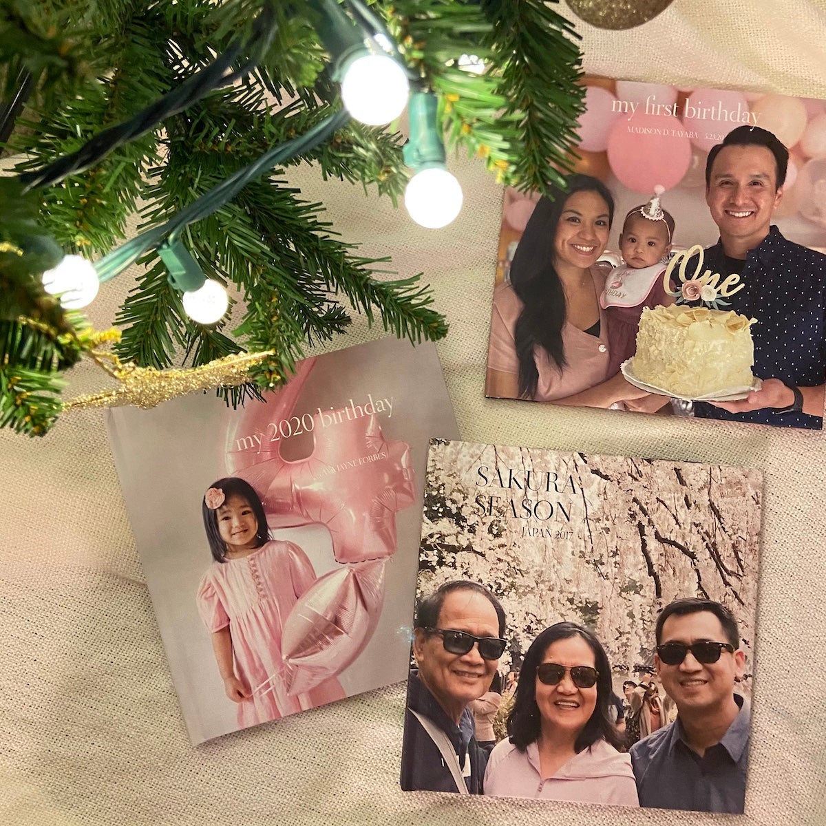 Multiple Artifact Uprising Photo-Wrapped Hardcover books commemorating birthdays resting under a Christmas tree with bulb lights