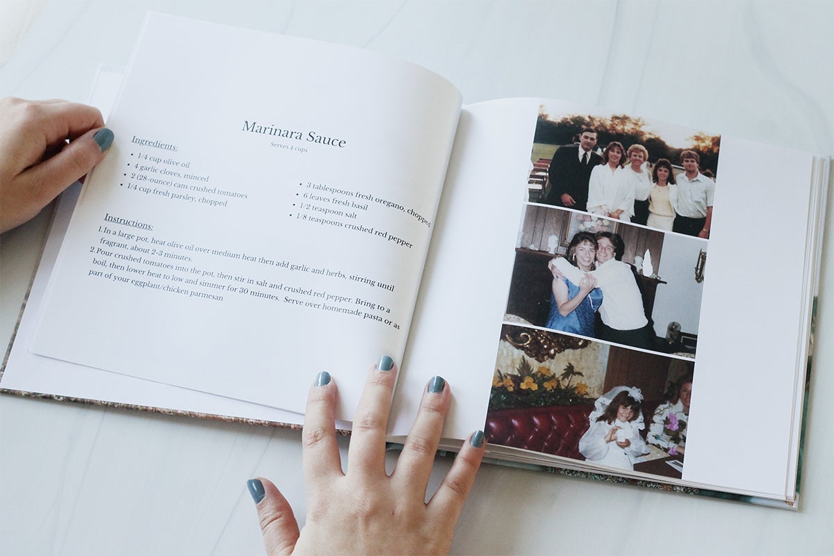 Custom family cookbook opened to recipe for Marinara Sauce on left page and family photos on right page