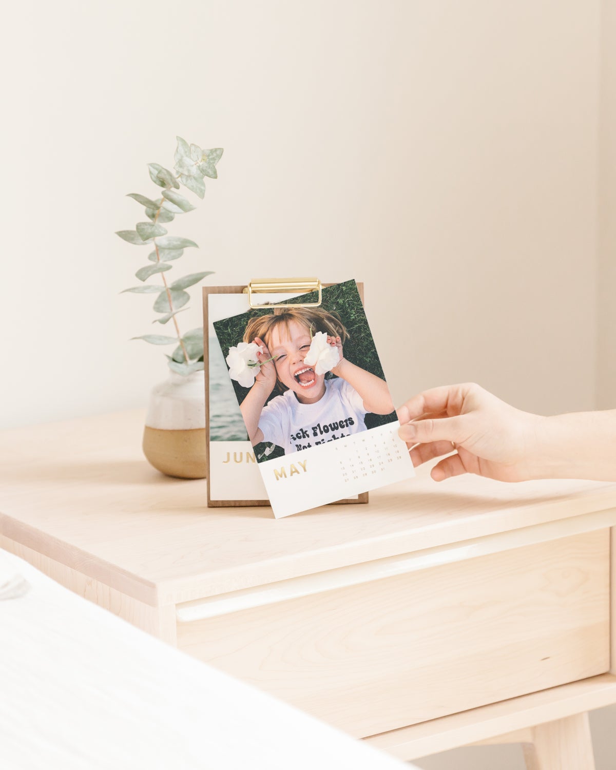 Desktop calendar on nightstand featuring playful photo of young child holding flowers