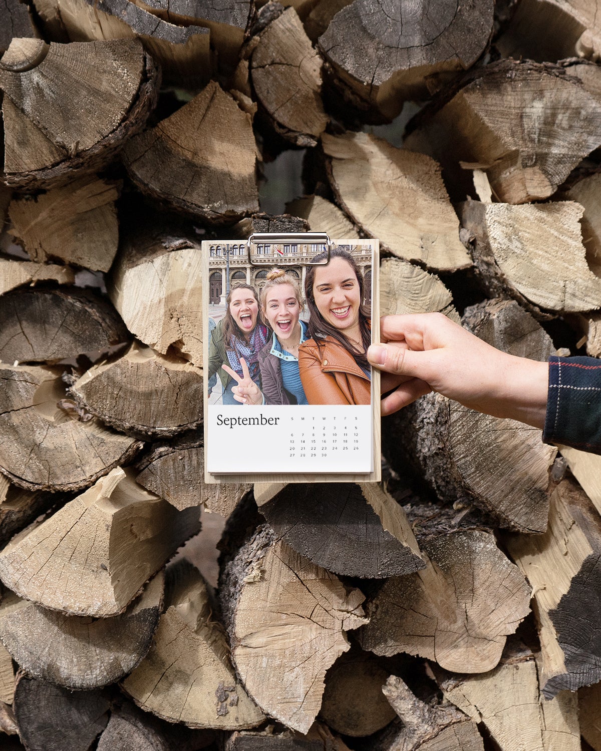 Hand holding up photo calendar with selfie of three friends featured