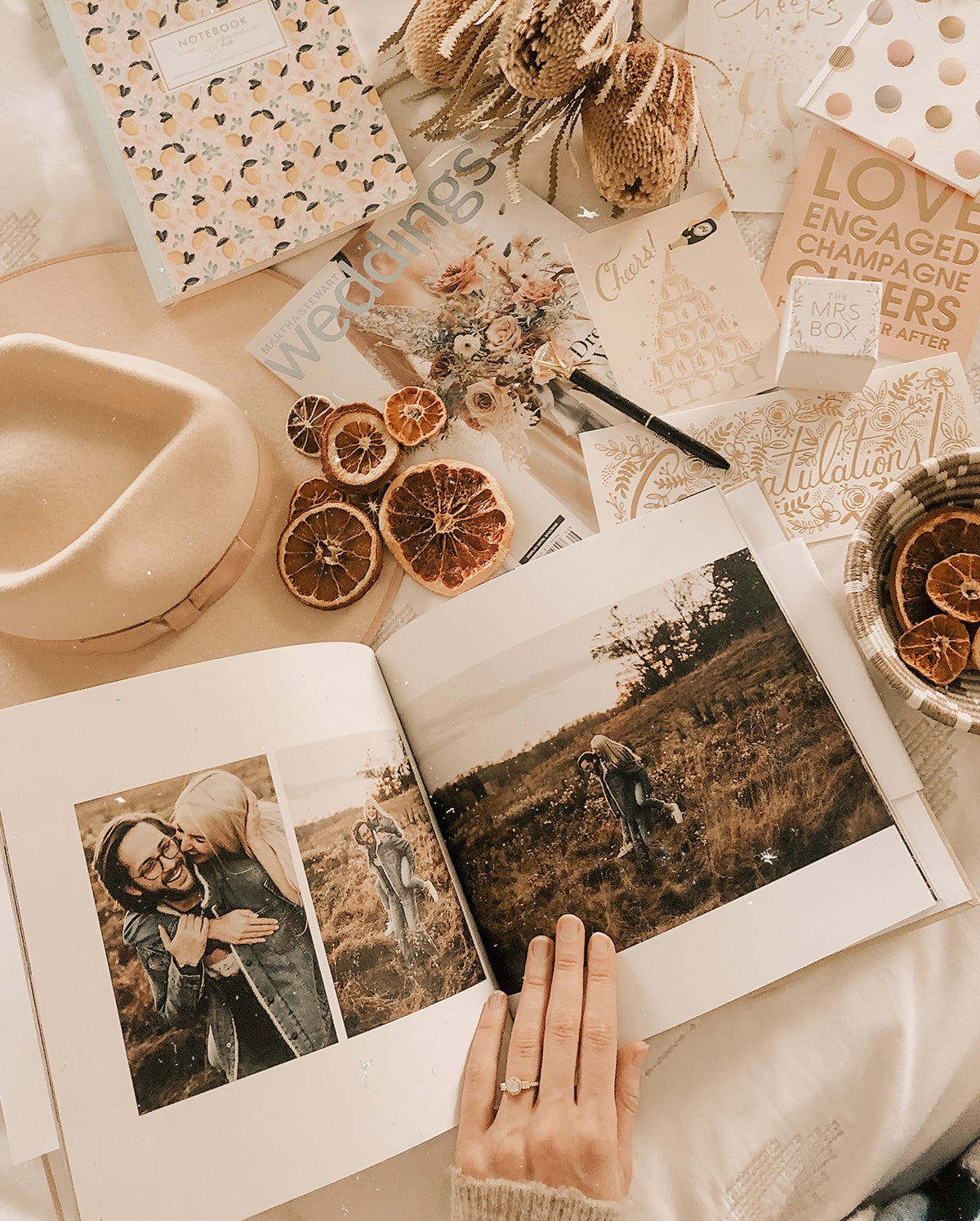 Artifact Uprising Hardcover Photo Book opened to engagement photos on table covered with wedding stationery and planning materials