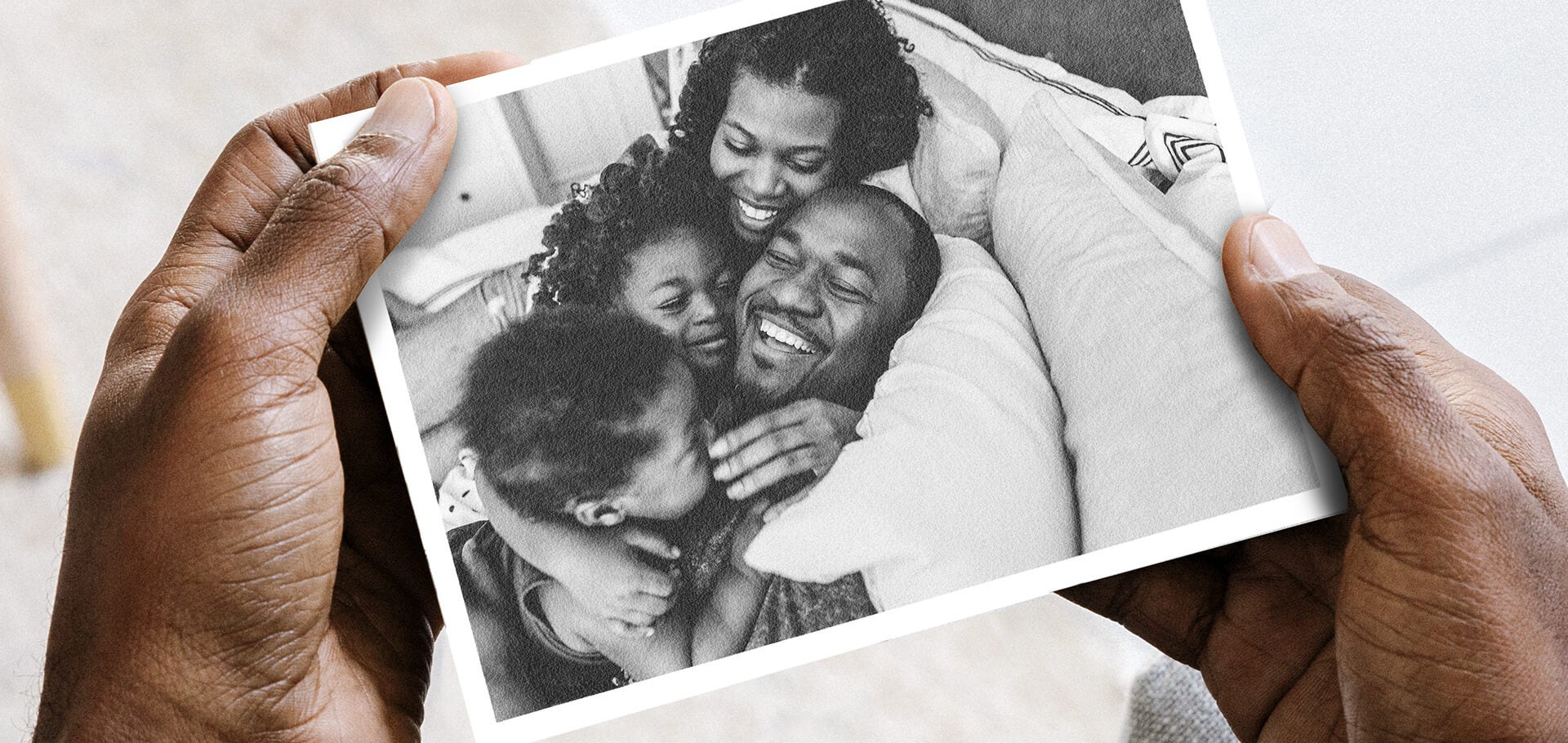 Hands holding DIY postcard with photo of family laughing and lounging on bed