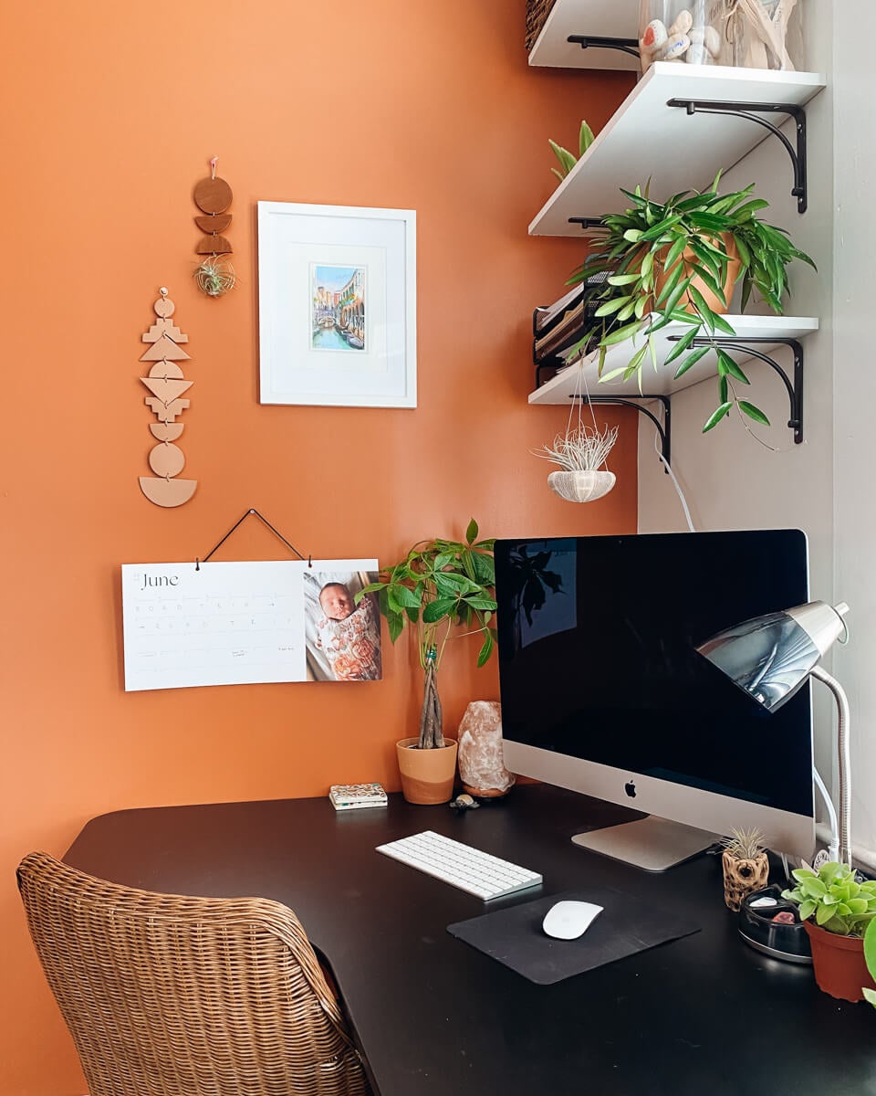 Home office featuring plants, orange wall, and Artifact Uprising Modern Wall Calendar