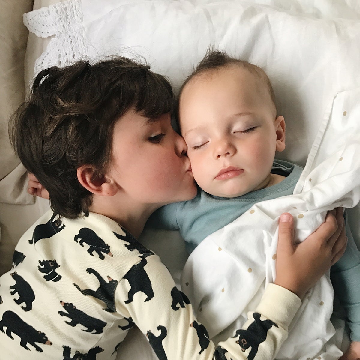 Little boy kissing his sleeping baby brother on the cheek