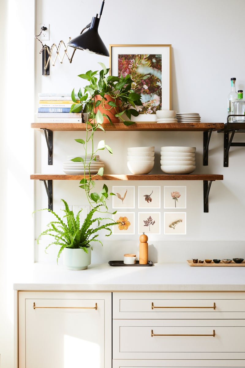 Kitchen shelves filled with small plants, framed photos, dishes, and photo prints