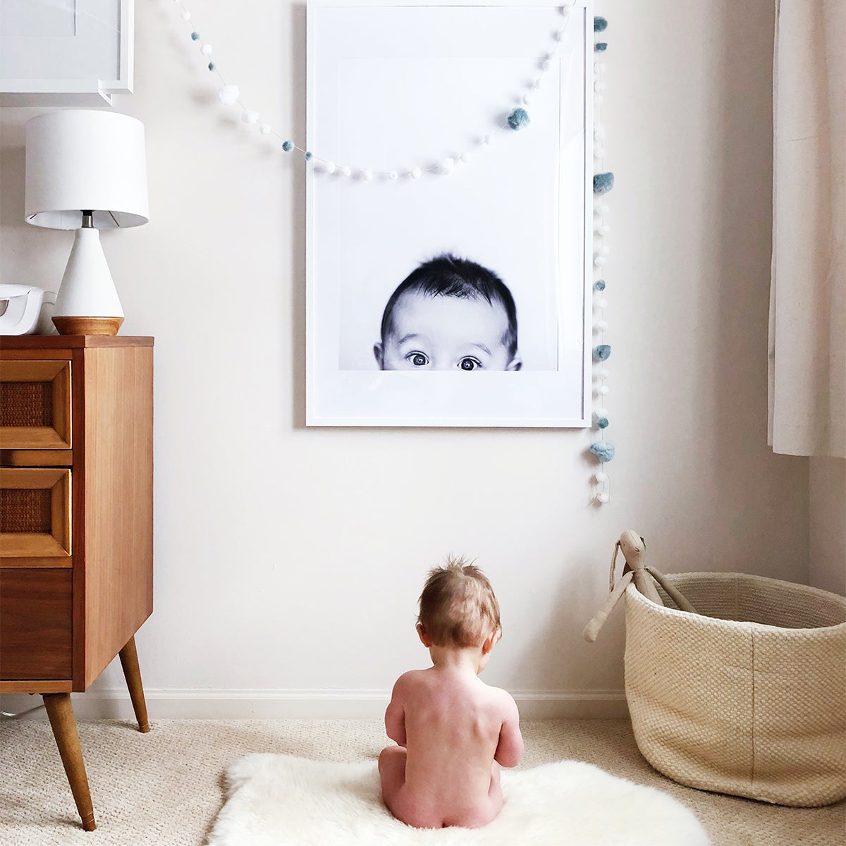 Baby sitting in front of enlarged photo of self on the wall