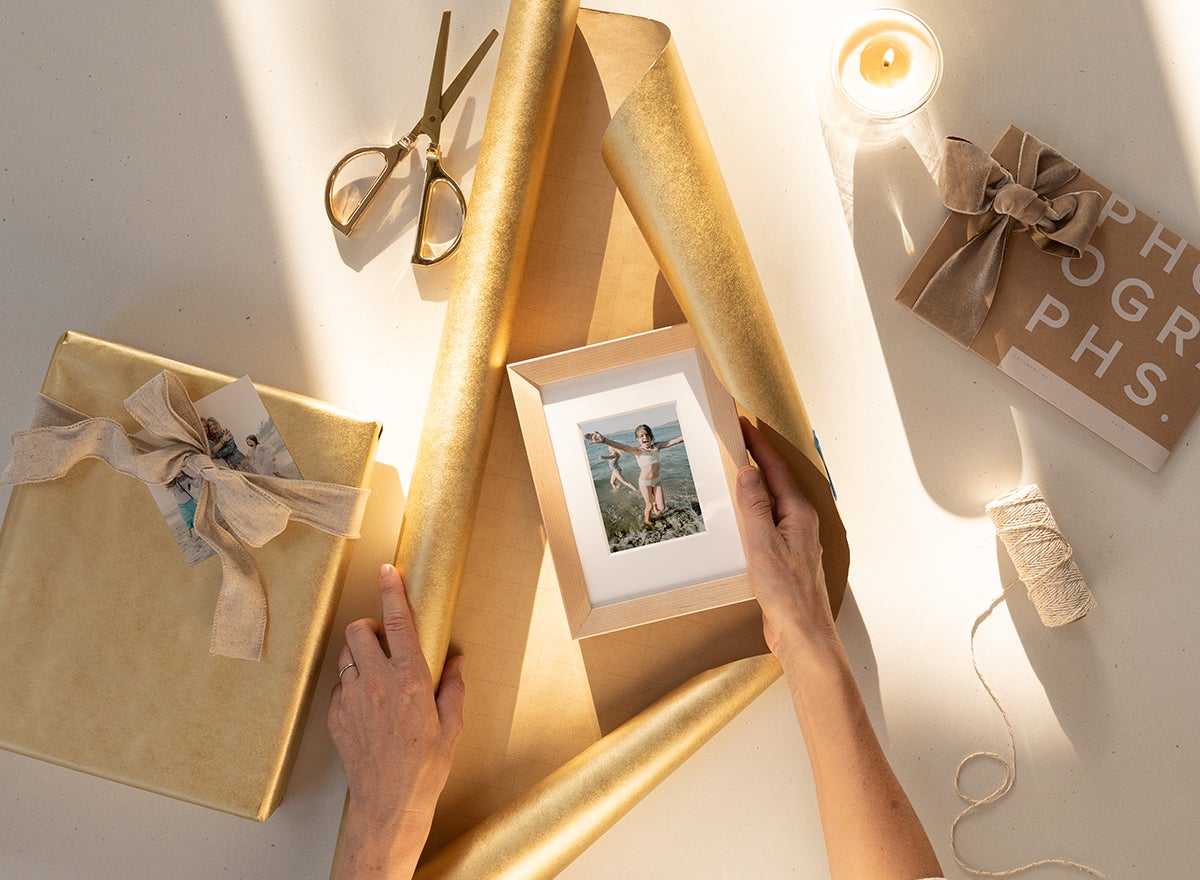 hands wrapping wooden tabletop photo frame in gold wrapping paper