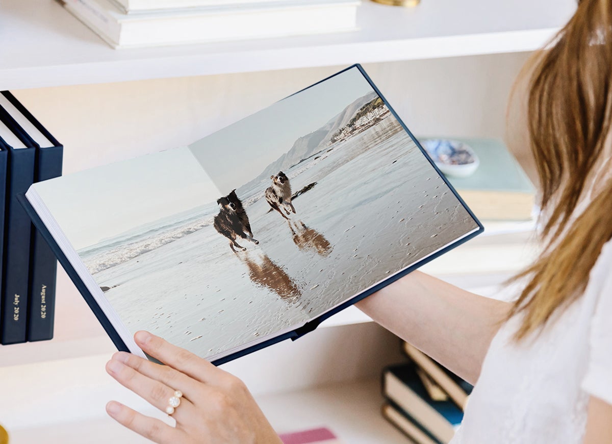 Woman holding Everyday Photo Book with panoramic spread of two dogs running along the beach