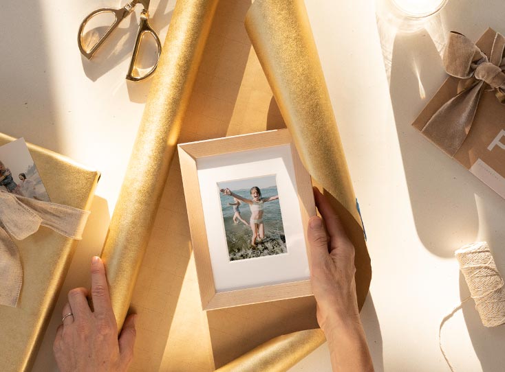 Framed photo of little girl being placed in the center of gold wrapping paper unfurled from tube