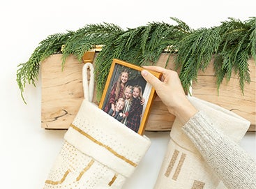 Hand slipping small framed photo into stocking hanging from mantel