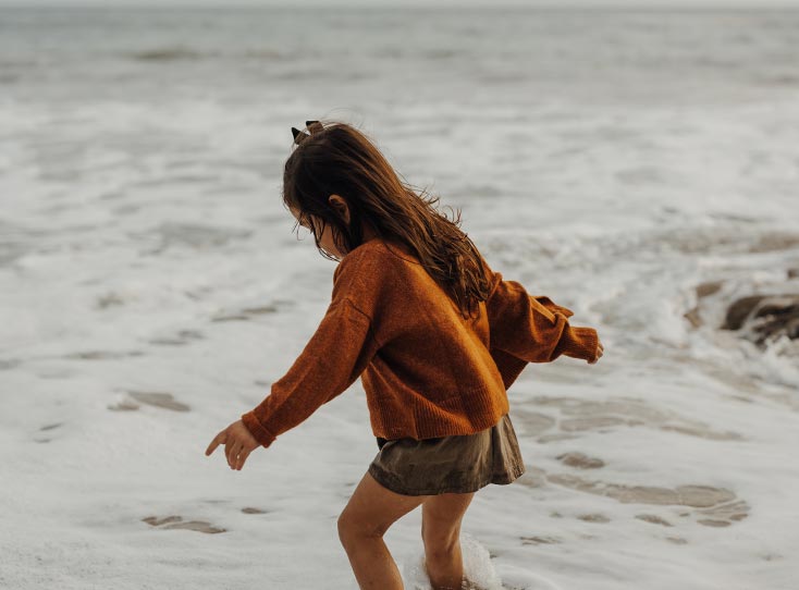 Little girl playing in coastal waters as the tide rolls in