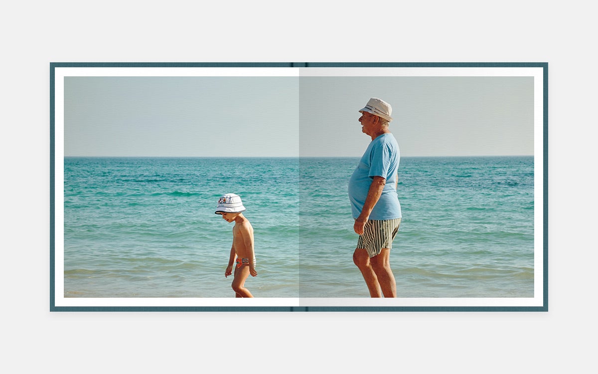 Two-page panoramic image in album of grandpa and little boy wearing matching hats and walking the beach