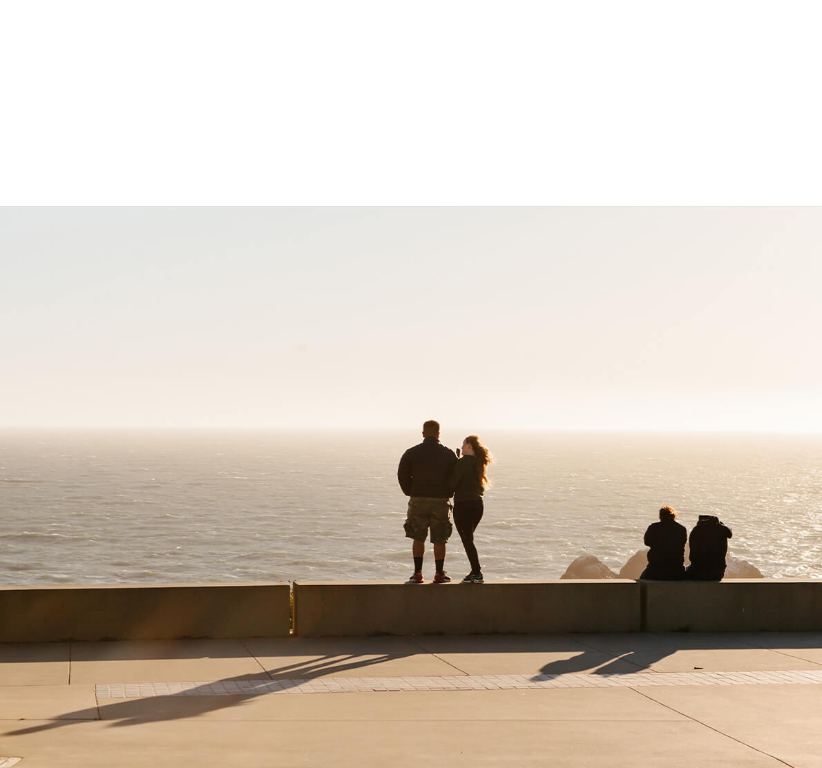 Photo by Brandon Lopez of couple standing on ledge by ocean