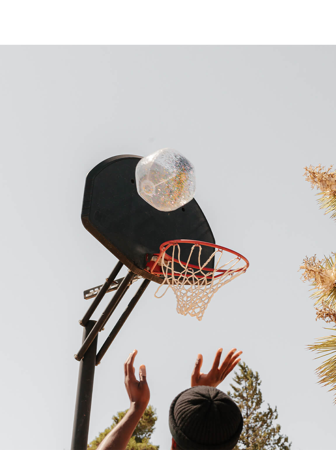 Photo by Brandon Lopez of hands shooting glittery beach ball into basketball hoop