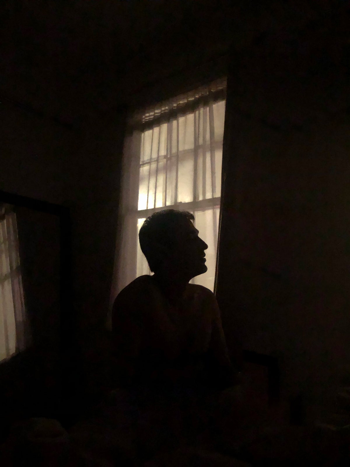Portrait of man's dimly lit silhouette in front of window