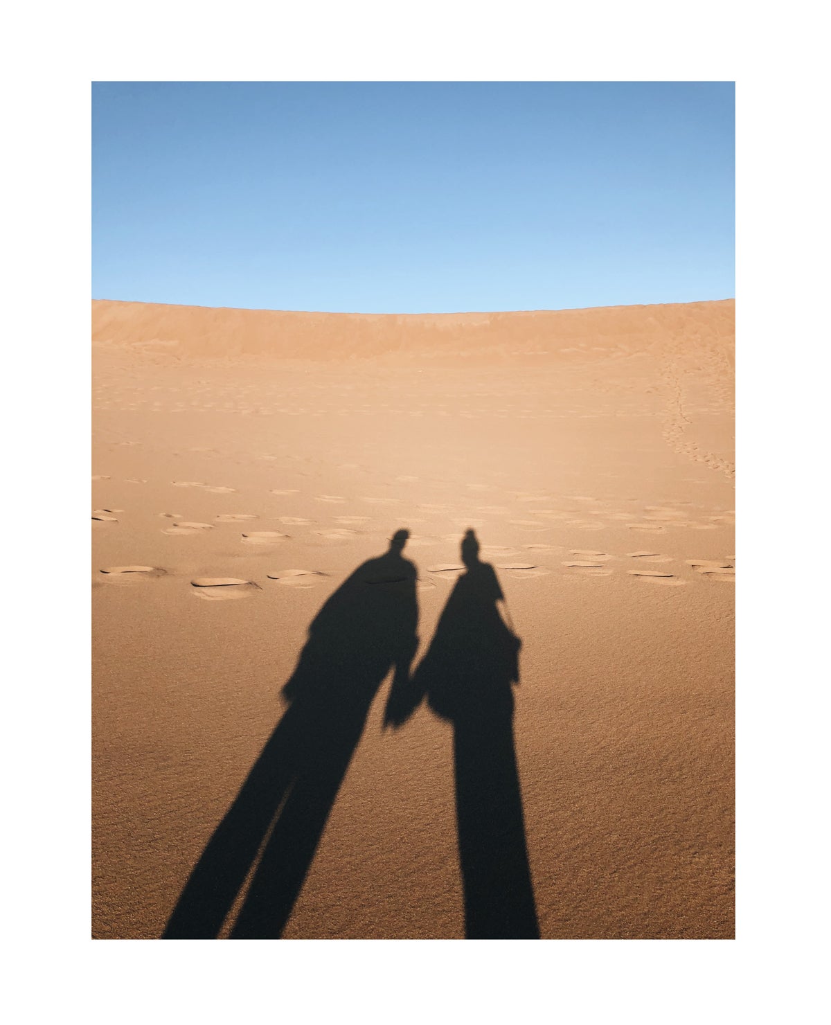 Photo of couple casting shadow onto desert sands by Molly Olwig