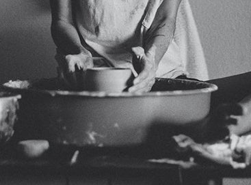 Black and white image of woman's hands throwing pottery on wheel